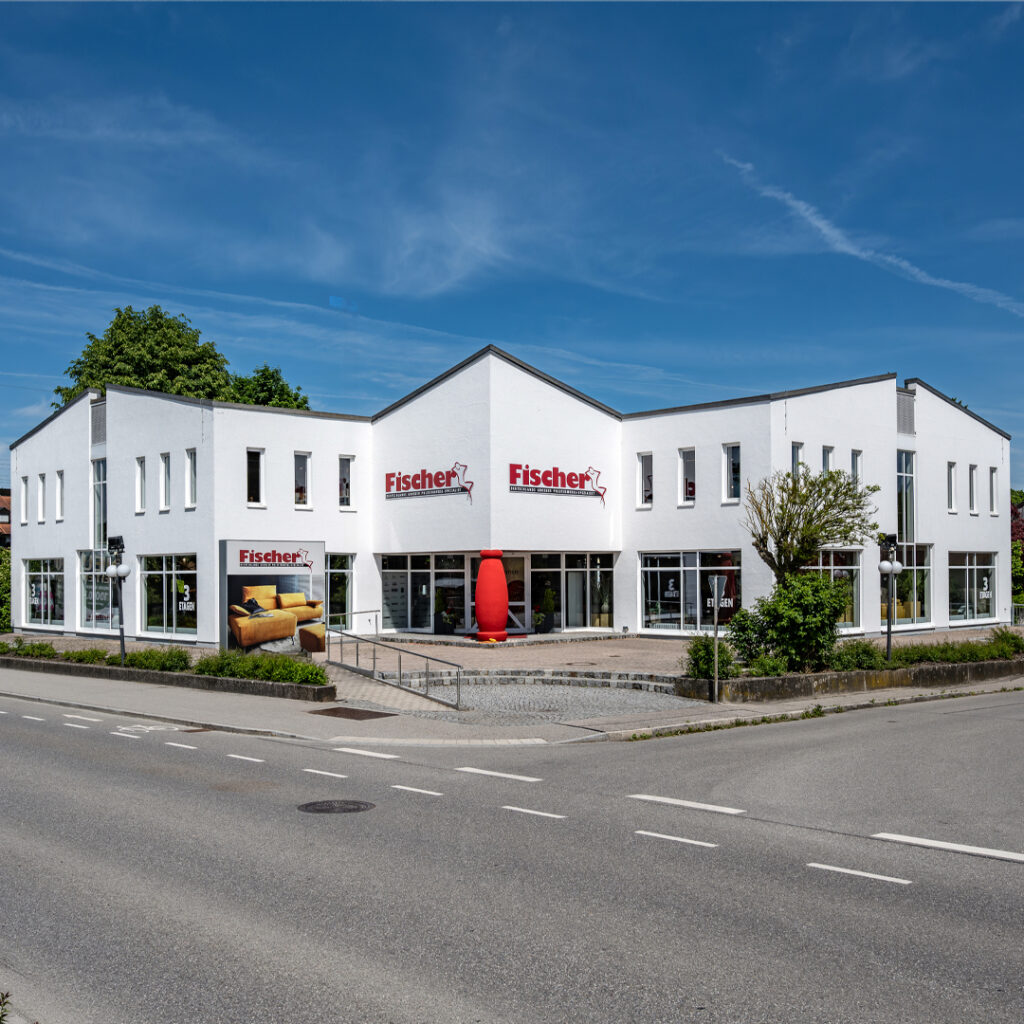 Polstermöbel Fischer Filiale in Neuötting mit weißem Eckgebäude, großem Schaufensterbereich und Möbelausstellung.